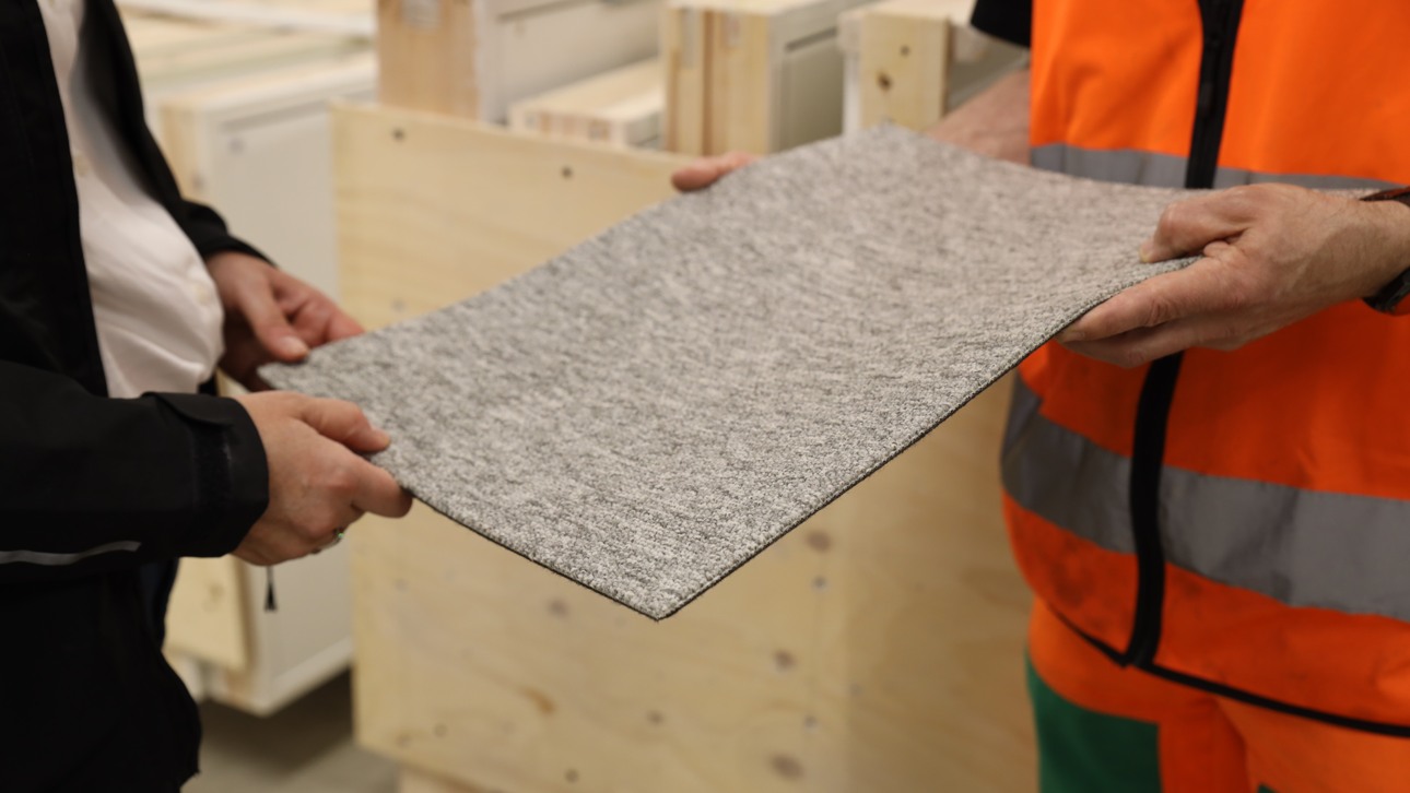 Two people holding a small piece of grey carpet between them at Ragn-Sells' reuse hub in Kista.